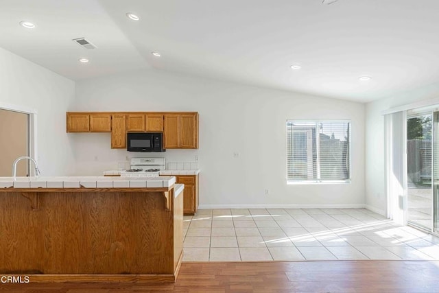 kitchen featuring tile countertops, visible vents, white range with gas cooktop, black microwave, and brown cabinets