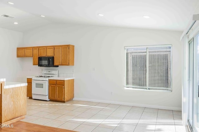 kitchen featuring visible vents, black microwave, tile counters, white range with gas stovetop, and brown cabinetry