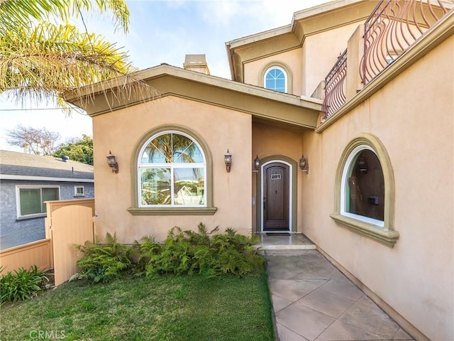 view of exterior entry featuring stucco siding, fence, and a gate