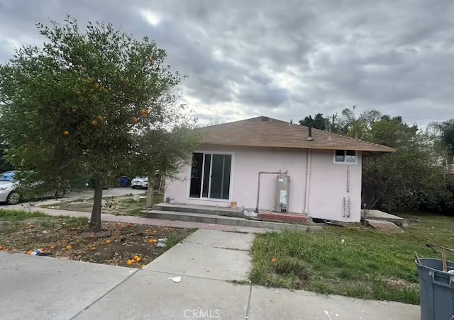 back of house with water heater and stucco siding