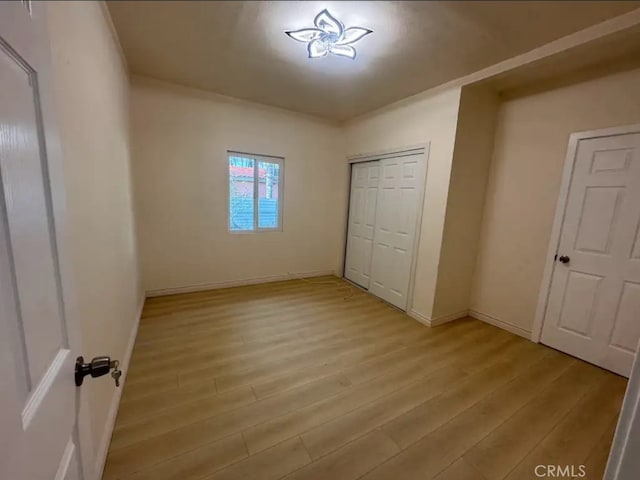 unfurnished bedroom with light wood-style flooring, baseboards, and a closet