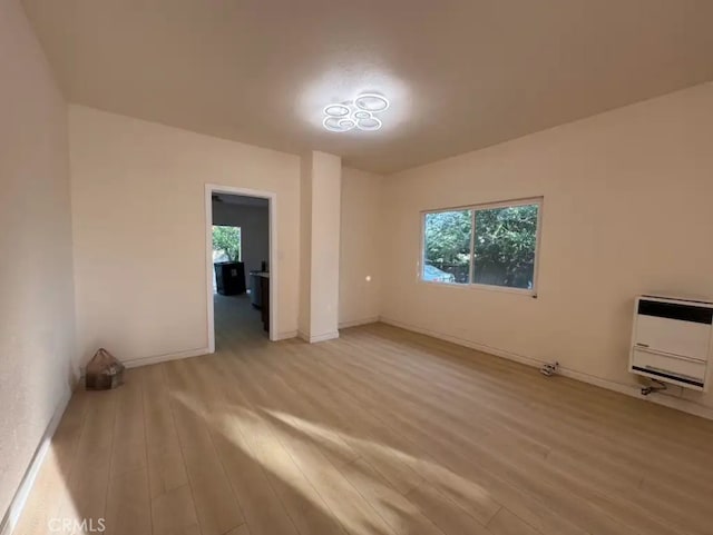 unfurnished room with heating unit, light wood-type flooring, and baseboards