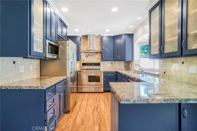 kitchen featuring blue cabinetry, stainless steel appliances, a peninsula, crown molding, and wall chimney range hood