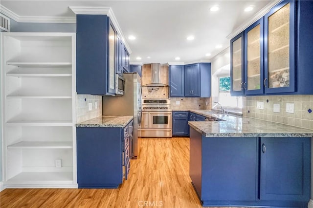 kitchen featuring light wood finished floors, blue cabinetry, wall chimney range hood, a peninsula, and stainless steel appliances