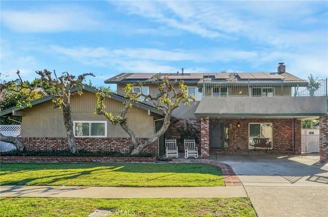 view of front facade featuring brick siding, solar panels, a front yard, stucco siding, and a balcony