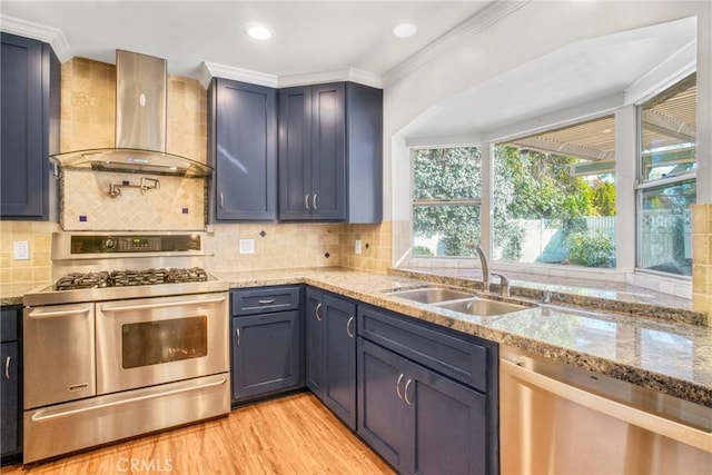 kitchen with light stone counters, stainless steel appliances, wall chimney range hood, and a sink