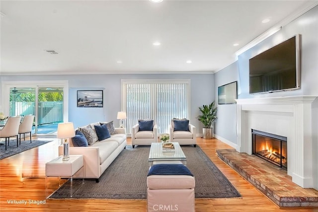 living room featuring wood finished floors, visible vents, baseboards, a glass covered fireplace, and crown molding