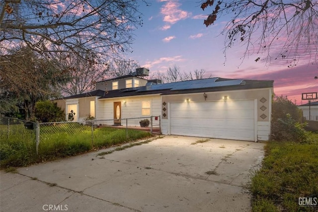 traditional home featuring a fenced front yard, roof mounted solar panels, a garage, and driveway