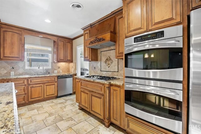 kitchen with tasteful backsplash, visible vents, brown cabinetry, stainless steel appliances, and a sink