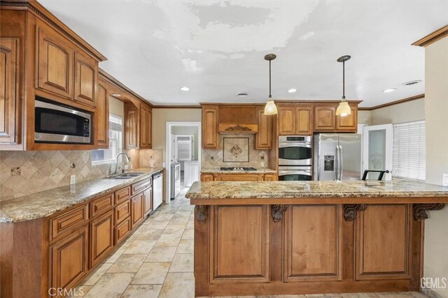 kitchen featuring light stone counters, a sink, appliances with stainless steel finishes, a kitchen bar, and brown cabinets