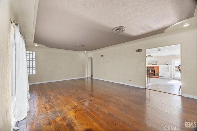 spare room featuring visible vents, arched walkways, baseboards, and hardwood / wood-style floors