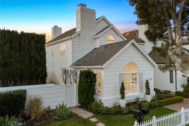 view of front of property with a shingled roof, a fenced front yard, and a chimney