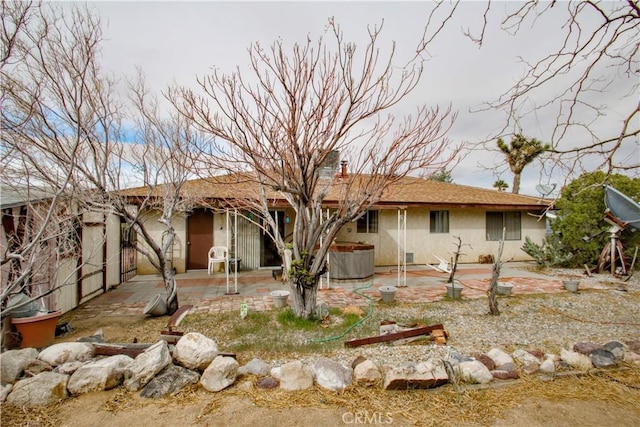 view of front facade featuring stucco siding, a patio, a chimney, and a hot tub