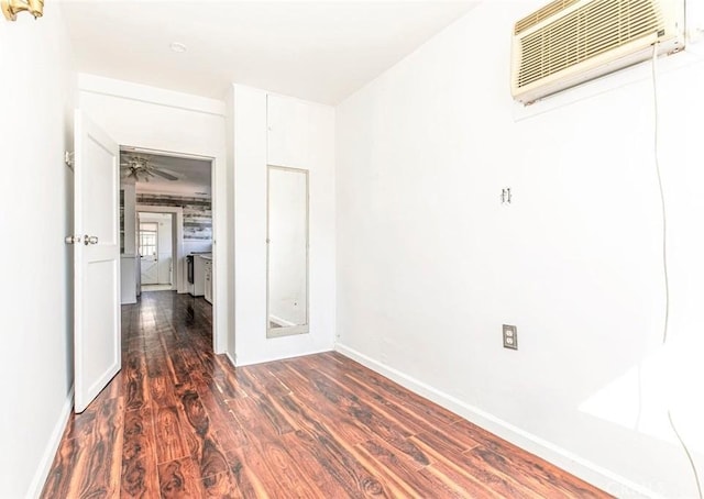 unfurnished room with a wall unit AC, baseboards, and dark wood-type flooring