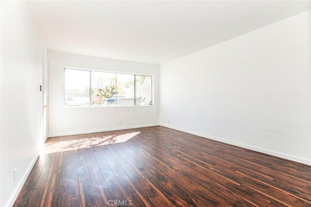 unfurnished room with dark wood finished floors and baseboards