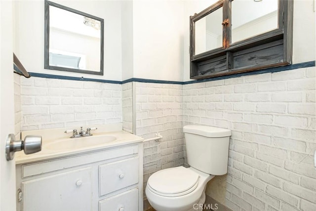 bathroom featuring vanity, toilet, tile walls, and wainscoting