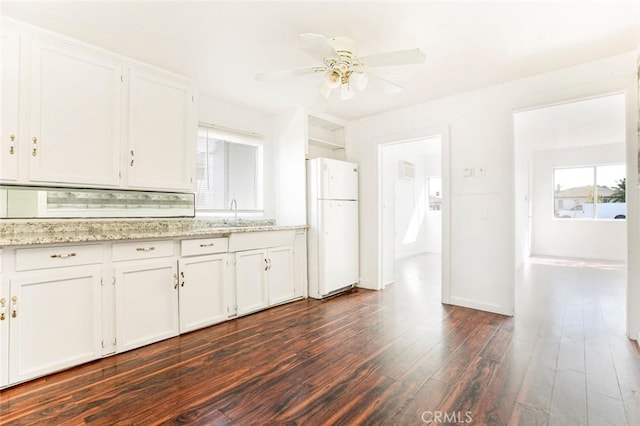 kitchen with dark wood-type flooring, a sink, white cabinetry, freestanding refrigerator, and light stone countertops