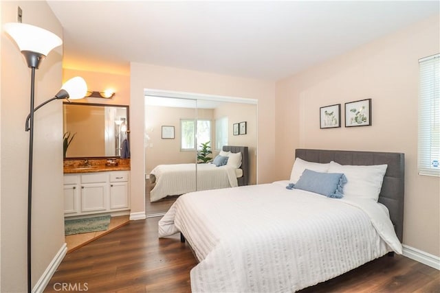 bedroom featuring a sink, baseboards, ensuite bath, and dark wood finished floors