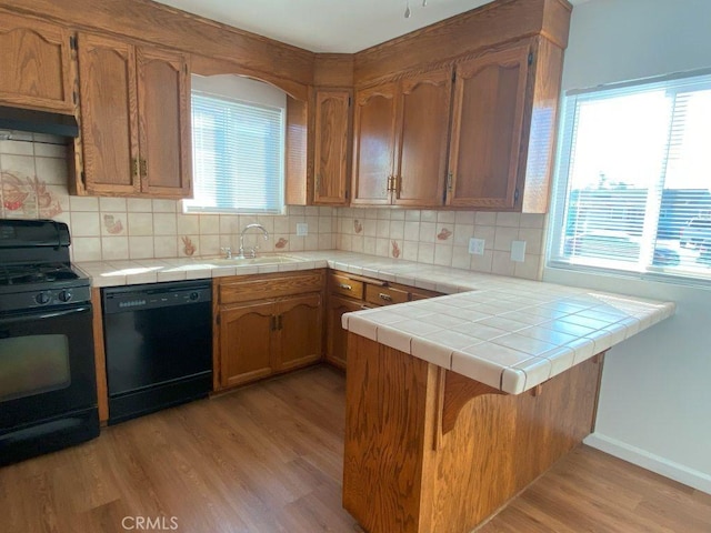 kitchen with a sink, black appliances, light wood-style floors, under cabinet range hood, and backsplash