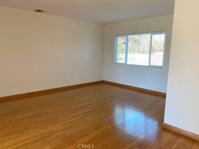 spare room featuring visible vents, baseboards, and wood finished floors