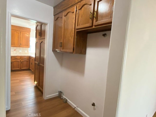 clothes washing area featuring light wood finished floors, cabinet space, and baseboards