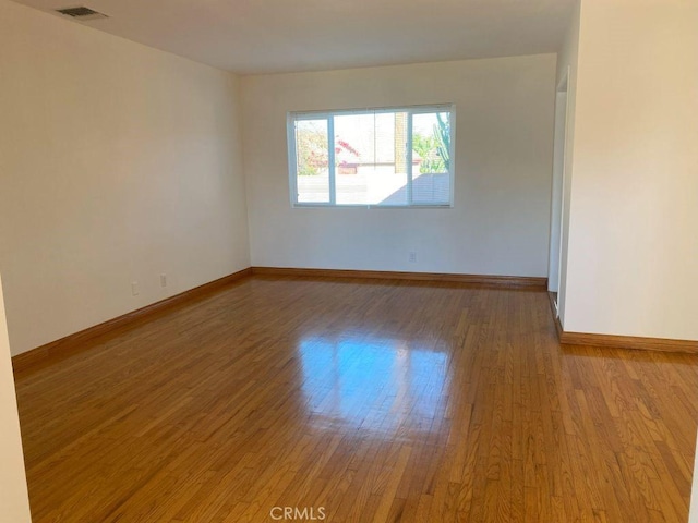 spare room with visible vents, baseboards, and wood finished floors