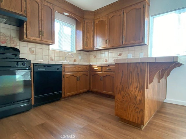 kitchen featuring black appliances, under cabinet range hood, tasteful backsplash, tile countertops, and light wood finished floors