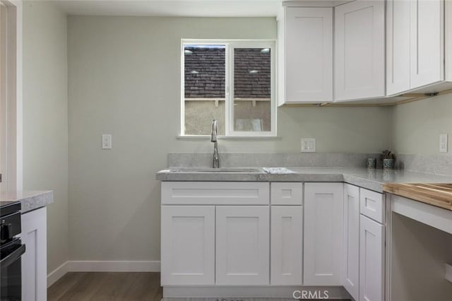 kitchen featuring a sink, wood finished floors, white cabinetry, light countertops, and baseboards