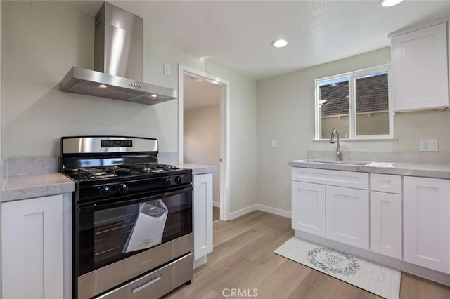 kitchen featuring light countertops, light wood-style flooring, stainless steel gas range, wall chimney exhaust hood, and a sink