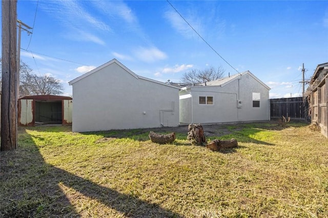 back of property featuring fence, stucco siding, an outdoor structure, a yard, and a storage unit