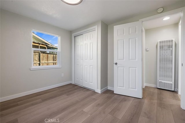 unfurnished bedroom with a heating unit, wood finished floors, baseboards, and a closet