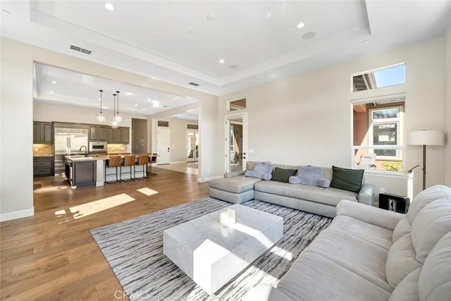 living room with visible vents, light wood-style flooring, baseboards, and a tray ceiling