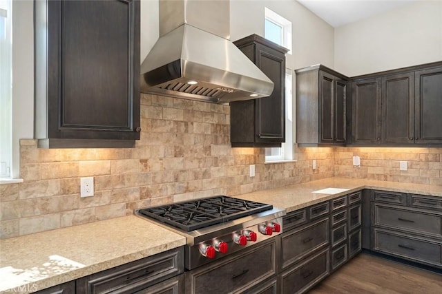 kitchen with backsplash, dark brown cabinetry, stainless steel gas stovetop, wall chimney exhaust hood, and dark wood-style flooring