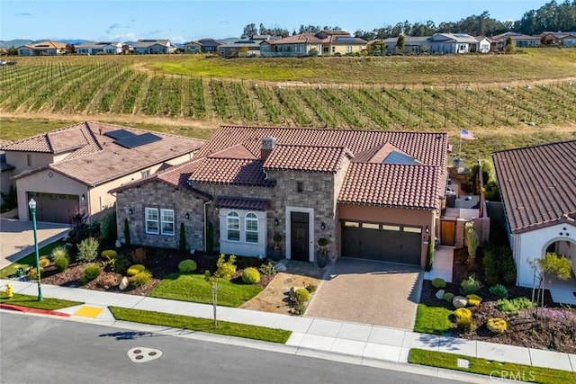 exterior space with a residential view, a tile roof, decorative driveway, stone siding, and an attached garage