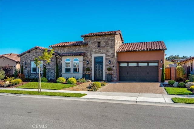 mediterranean / spanish-style home featuring a tiled roof, stucco siding, decorative driveway, a garage, and stone siding