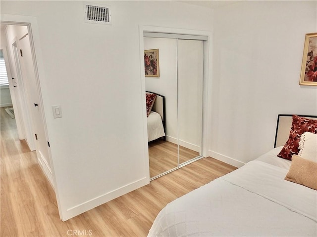 bedroom featuring light wood-style flooring, baseboards, visible vents, and a closet