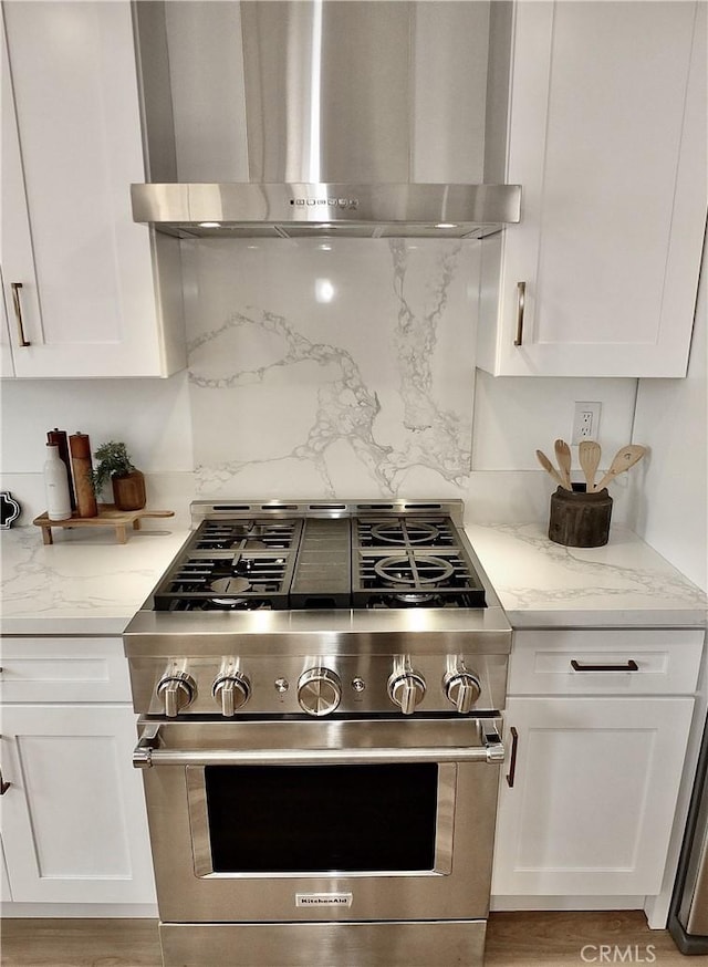 kitchen featuring stainless steel stove, white cabinets, and wall chimney exhaust hood