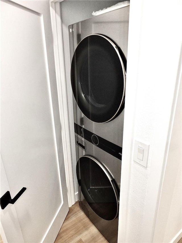 clothes washing area with laundry area, light wood-style flooring, and stacked washer and clothes dryer