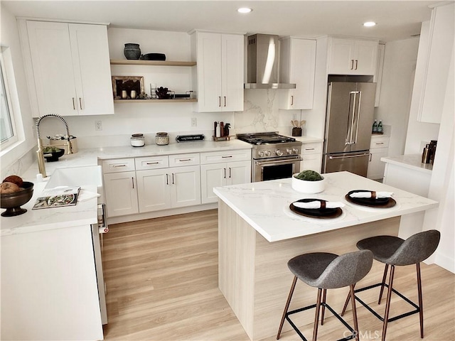 kitchen with a kitchen breakfast bar, high end appliances, light wood-style floors, wall chimney exhaust hood, and a sink