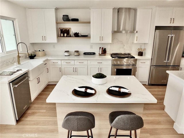 kitchen with high quality appliances, a breakfast bar, open shelves, white cabinetry, and wall chimney exhaust hood