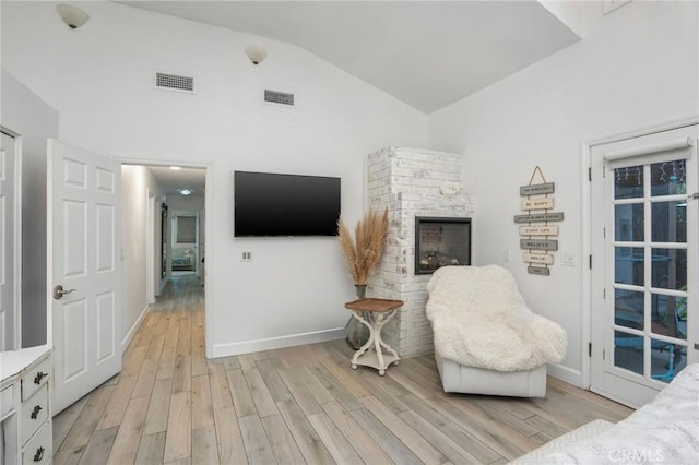 interior space featuring visible vents, a fireplace, light wood-style floors, and vaulted ceiling