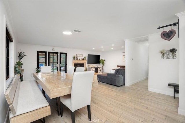 dining area with visible vents, light wood finished floors, baseboards, a fireplace, and crown molding