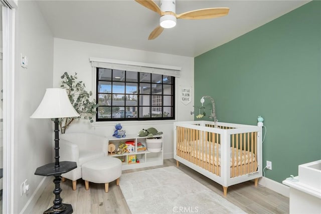 bedroom featuring a crib, a ceiling fan, baseboards, and wood finished floors