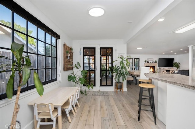 interior space with recessed lighting, french doors, a lit fireplace, and light wood finished floors