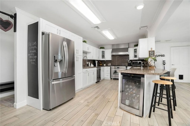 kitchen featuring backsplash, glass insert cabinets, wine cooler, stainless steel appliances, and wall chimney exhaust hood