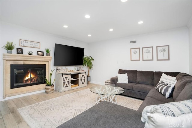 living area featuring visible vents, ornamental molding, a glass covered fireplace, wood finished floors, and recessed lighting