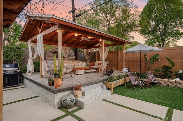 patio terrace at dusk with area for grilling, a fenced backyard, ceiling fan, a gazebo, and an outdoor hangout area