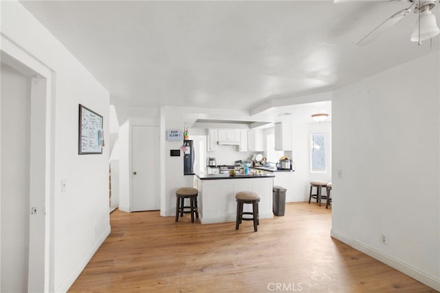 kitchen featuring light wood-type flooring, a kitchen bar, dark countertops, white cabinets, and ceiling fan