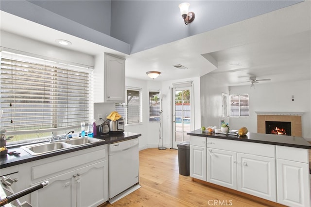 kitchen with dark countertops, a tiled fireplace, dishwasher, light wood-style flooring, and a sink