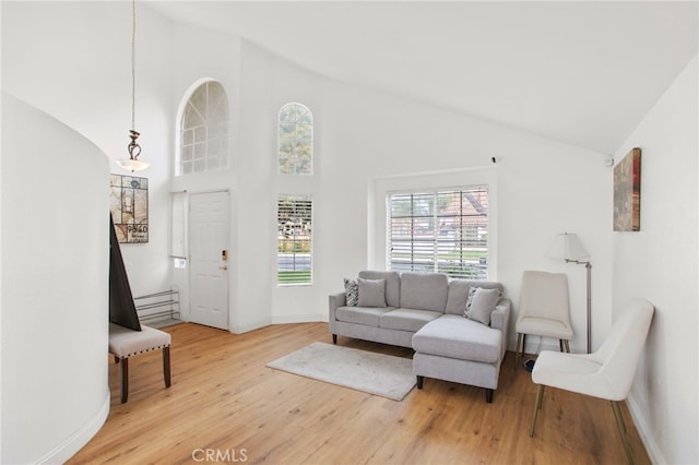 living area with baseboards, high vaulted ceiling, and light wood-style flooring